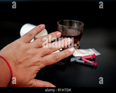 Eine Person und deutete mit der Hand stoppen, Drogen, Pillen in verschiedenen Größen, Formen und Farben, ein Glas Whiskey, Medikamente und Spritzen Konzept von Drogen und Stockfoto