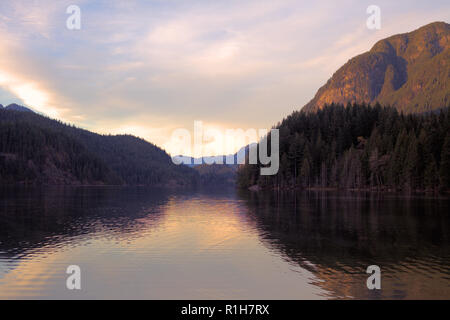 Buntzen Lake, in Anmore, BC, Kanada, bei Sonnenuntergang mit Wolken, beleuchteten Berge von Koniferen, und der Reflektierende heitere Wasser Stockfoto