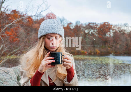 Schöne Frau in warme Kleidung und Strickmütze Kaffee trinken im Herbst Park. Frau mit Becher Kaffee in der Hand outdoor. Stockfoto