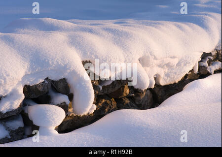 Verschneite alte Steinmauer von einem niedrigen Winkel Sonne beleuchtet. Stockfoto