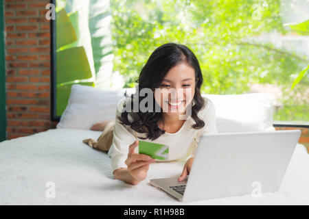 Eine Frau lächelt und auf der Suche vor ihr, wie sie ihre Kreditkarte mit ihrem Laptop nutzt. Stockfoto