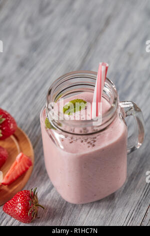 Milch Smoothie mit Erdbeeren, Minze und Chia Samen in ein Glas mit Strohhalm auf einem Holztisch mit kopieren. Gesundes Getränk Stockfoto