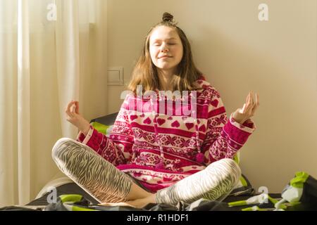 Jugendmädchen meditieren und lächelnd, während im Yoga pose sitzen auf dem Bett. Stockfoto