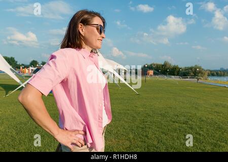 Frau mittleren Alters genießt einen Urlaub im Sommer Erholung Zone, weiblichen draußen heben die Hände im Sonnenlicht Park. Stockfoto