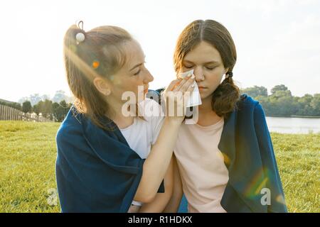 Junges Mädchen tröstet sie weinen, wütend, traurig, Freund. Die Mädchen sitzen auf dem grünen Rasen im Park. Stockfoto