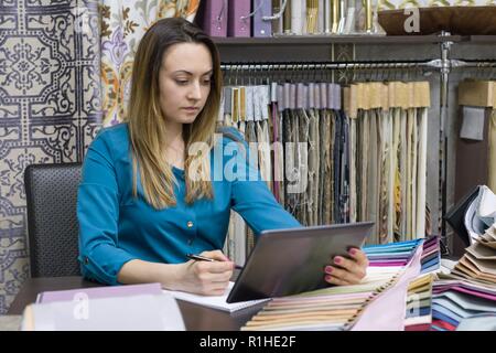 Small Business, Shop, Show room von Stoffen und Zubehör für den Innenraum. Frau sieht eine digitale Tablet, wählt aus Stoffen, zeichnet Skizzen von Inter Stockfoto