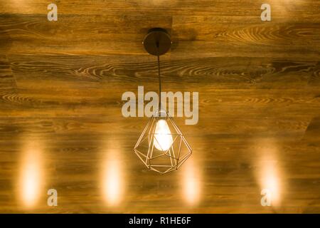 Moderne, elegante geometrische Lampe auf einer bronzenen braunen Holzdecke. Stockfoto