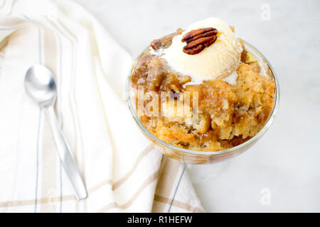 Pecan Cobbler mit Vanilla Ice Cream: Ein Gericht aus südlichem Pekannuskuchen in einer Glas Dessertschüssel mit einem Löffel Stockfoto