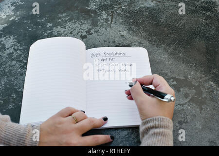 Frau Hände schreiben neue Jahre Auflösungen für 2019 in einer Zeitschrift Stockfoto