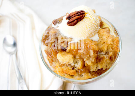 Pecan Cobbler mit Vanilla Ice Cream: Ein Gericht aus südlichem Pekannuskuchen in einer Glas Dessertschüssel mit einem Löffel Stockfoto