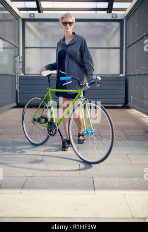 In voller Länge Bild des blonden Jungen mit grünen Fahrrad in der Nähe der graue Wand während des Tages Stockfoto