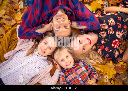 Foto von oben der Lüge Eltern mit Kindern auf gelbe Blätter im Park am Nachmittag Stockfoto