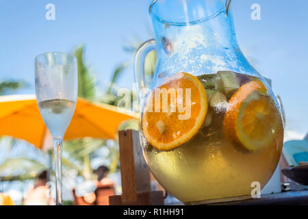 Blick auf die Terrasse der Bar mit Glas und Glas Sangria im Fokus und Hintergrund mit Sonnenschirm, Himmel und Palmen, in Angola Stockfoto