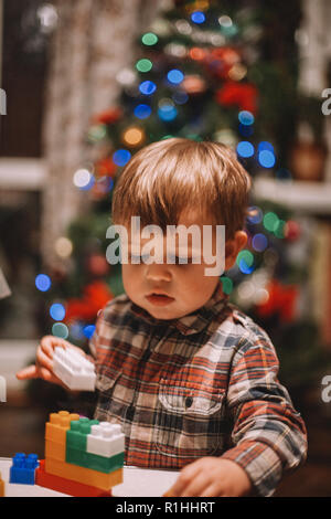 Baby Boy zu Hause spielt während der Weihnachtsfeiertage gegen Weihnachtsbaum Stockfoto