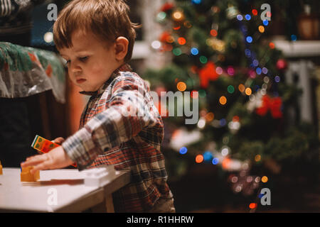 Baby Boy zu Hause spielt während der Weihnachtsfeiertage gegen Weihnachtsbaum Stockfoto