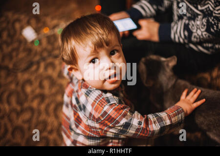 Portrait von baby boy mit Kamera auf dem Fußboden sitzen zu Hause mit seiner Mutter und seiner Katze Stockfoto