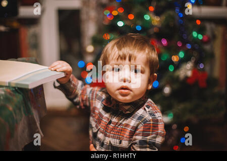 Baby Boy holding Buch, während gegen Weihnachtsbaum zu Hause stehend Stockfoto