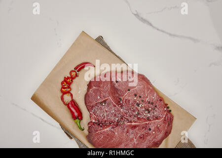 Ansicht von oben frisches rohes Fleisch auf Backpapier mit gehackten Chili auf weißem Hintergrund Stockfoto