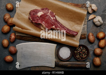 Flach mit raw-Rib Eye Steak auf Backpapier mit fleischermesser, Gewürze, Kartoffeln und Knoblauch Stockfoto