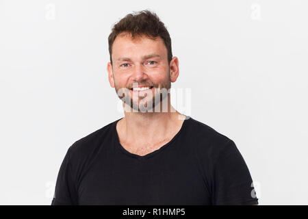 Stattlicher Mann mit schwarzen Shirt mit schönen Lächeln gegen den weißen Hintergrund posiert Stockfoto