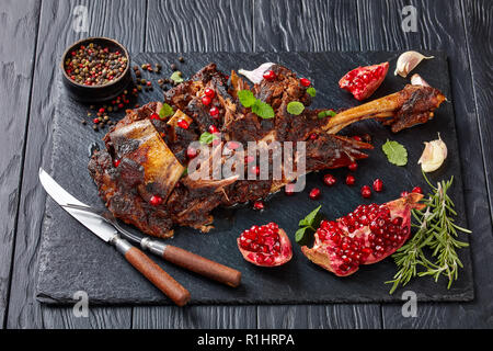 Lecker gebratene Lammkeule mit Gewürzen und Rosmarin auf schwarzem Schiefer Platte auf einem Holztisch, Ansicht von oben, close-up Stockfoto