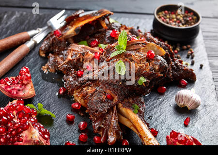 Köstliche langsam gekochte Lammkeule mit Granatapfel Samen, Minze, Gewürze und Rosmarin auf schwarzem Schiefer Platte auf einem Holztisch, Ansicht von oben, c Stockfoto