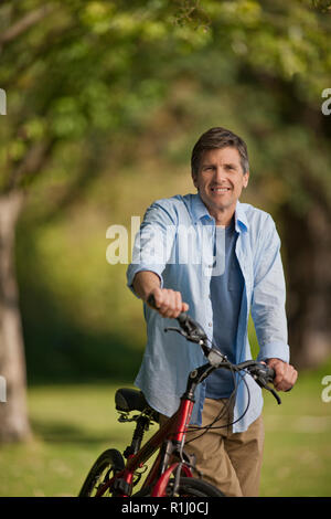 Porträt eines lächelnden Mann mittleren Alters sein Fahrrad in einem Park. Stockfoto