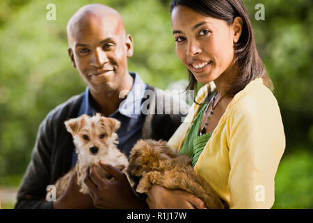 Junge heterosexuellen Paaren, Lächeln, als sie Welpen halten und für ein Portrait darstellen. Stockfoto