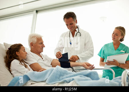 Ältere Menschen, die einen Besuch im Krankenhaus von seiner Enkelin, während mit seinen Blutdruck. Stockfoto