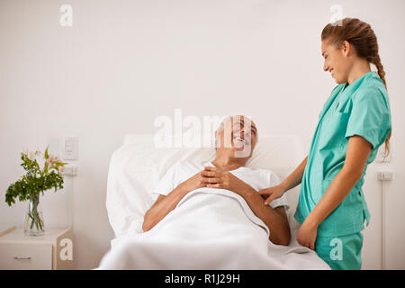 Weibliche Krankenschwester Lachen mit älteren männlichen Patienten im Krankenhaus Bett lag. Stockfoto
