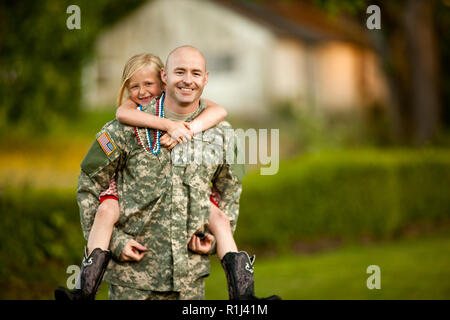 Lächelnd männlichen Soldaten piggy-backing seine junge Tochter in ihrem Hinterhof. Stockfoto