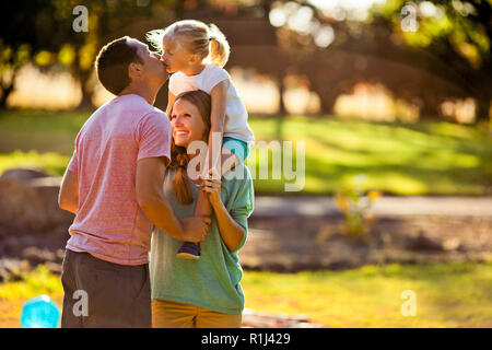 Glückliche junge Mädchen sitzen auf ihrer Mutter Schultern und küsste ihre Vater. Stockfoto