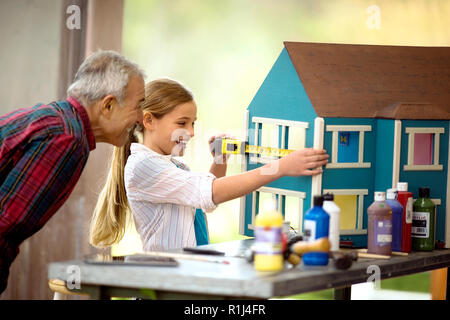 Lächelnden jungen Mädchen eine Puppe Haus, während ihr Großvater auf aussieht. Stockfoto