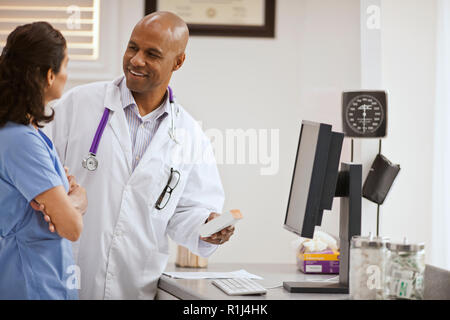 Lächelnd männlicher Arzt ein Gespräch mit einem weiblichen Krankenschwester über eine Box der Medikation in seinem Büro. Stockfoto