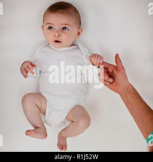 Süß lächelnde Baby Boy und schaut aus seinem Kinderbett, als er seine Mutter fingerfest schließen. Stockfoto