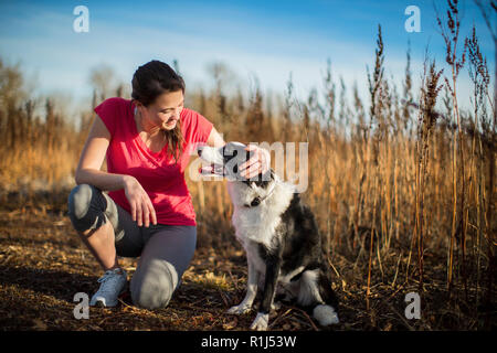 Lächelnden jungen Frau kniet und Haustiere Hund, wie Sie sich vorbereiten für einen Lauf in die Landschaft zu gehen. Stockfoto