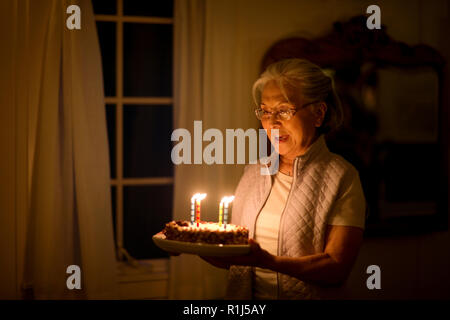 Ältere Frau mit einem Geburtstagskuchen mit Geburtstag Kerzen dekoriert. Stockfoto