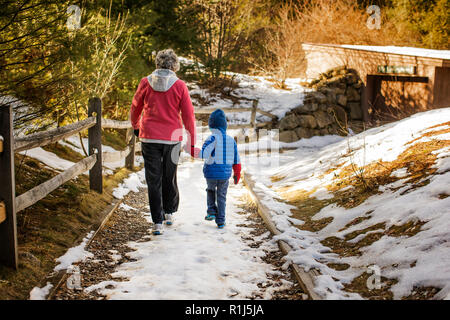 Großmutter und Enkel gingen Hand in Hand an einem verschneiten Fußweg. Stockfoto