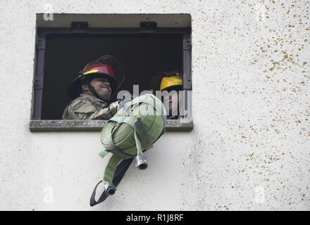 Flieger vom 422Nd Sicherheitskräfte Squadron ein Brand den Schlauch nach oben der Seite einer Ausbildung Turm während einer Feuerwehrmänner Herausforderung an RAF Croughton, England am Okt. 5, 2018 ziehen. Die Herausforderung war Teil der Kick-off-Veranstaltung für den vorbeugenden Brandschutz Woche die jährlich im Oktober in einer Bemühung, die Gemeinschaft über den Brandschutz und Vorbeugung zu informieren. Stockfoto