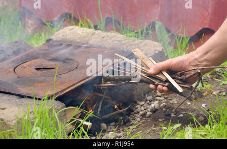 Die menschliche Hand Holz- Splitter Feuer in einem vintage Herd zu setzen Stockfoto