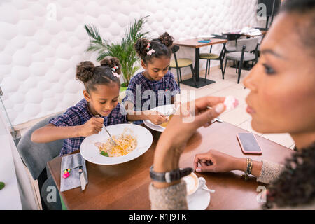 Dunkelhaarige Mutter Gefühl nachdenklich, während ihre Kinder beim Mittagessen Stockfoto