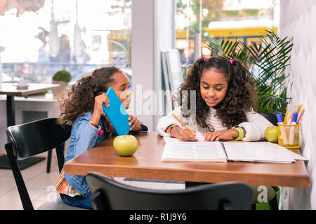 Zwei lockigen dunkelhaarigen Schwestern am Tisch sitzen und zusammen studieren Stockfoto