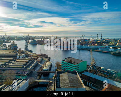 Antenne; drone Aussicht auf Port mit Werft Silhouetten am Horizont; industrielle Stadtlandschaft bei sonnigem Wetter mit blauem Himmel; Prozess der Reparatur von Schiffen, l Stockfoto