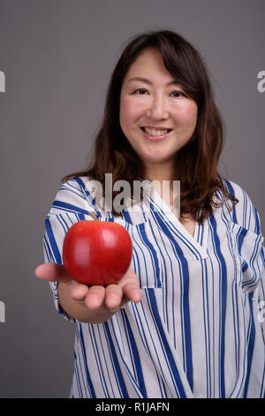 Reifen schöne asiatische Geschäftsfrau hält gesund Apple Stockfoto