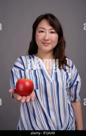 Reifen schöne asiatische Geschäftsfrau hält gesund Apple Stockfoto