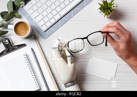 Zugeschnittenes Bild der Geschäftsmann mit Cyborg hand Brillen am Tisch mit leeren besuchen Sie Karten und Tastatur des Computers im Büro Stockfoto