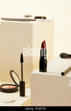 Nahaufnahme von roten Lippenstift mit verschiedenen Make-up Zubehör auf beige Würfel Stockfoto