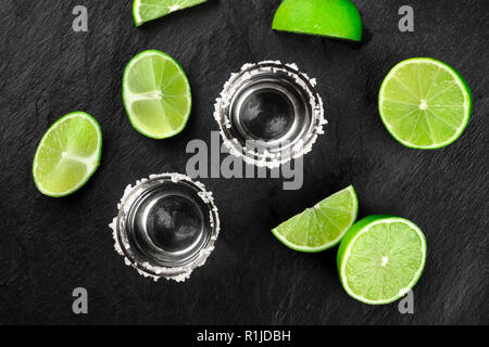Zwei tequila Schüsse mit vielen Kalk Scheiben, geschossen von oben auf einen dunklen Hintergrund Stockfoto