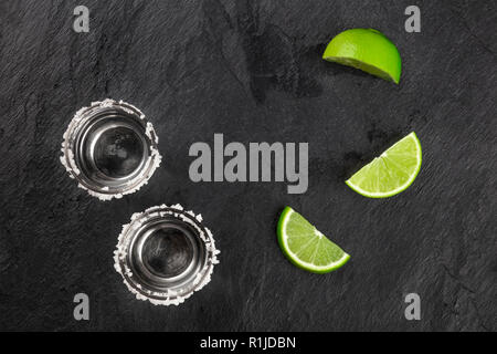 Ein Foto von zwei tequila Schüsse mit Kalk, Scheiben, geschossen von oben auf einem dunklen Hintergrund mit einem Platz für Text Stockfoto
