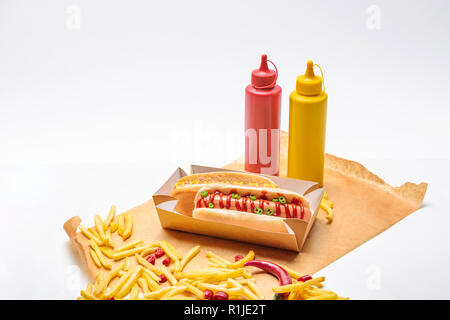 Nahaufnahme von Hot Dogs mit Pommes frites, Senf und Ketchup auf Papier auf weiße Oberfläche Stockfoto